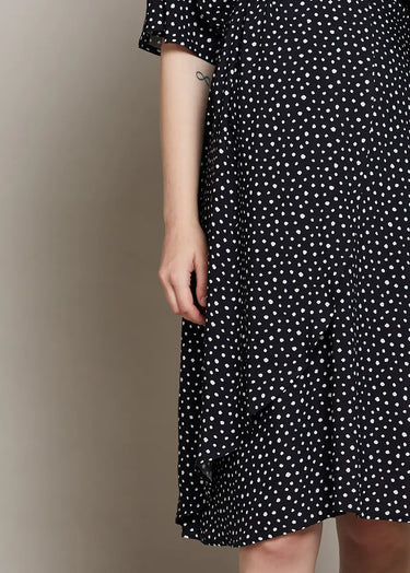 Black dress with white polka dot pattern worn by a person on a beige background